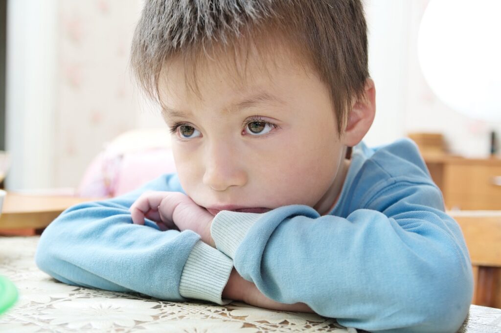 Retrato de un niño triste que mira hacia otro lado pensando sentado en la mesa, un niño pensativo que se siente herido